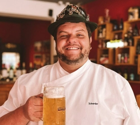Homem sorrindo segurando copo de cerveja dentro de restaurante