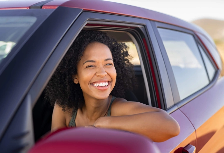 Mulher sorridente olha para fora da janela de um carro vermelho.