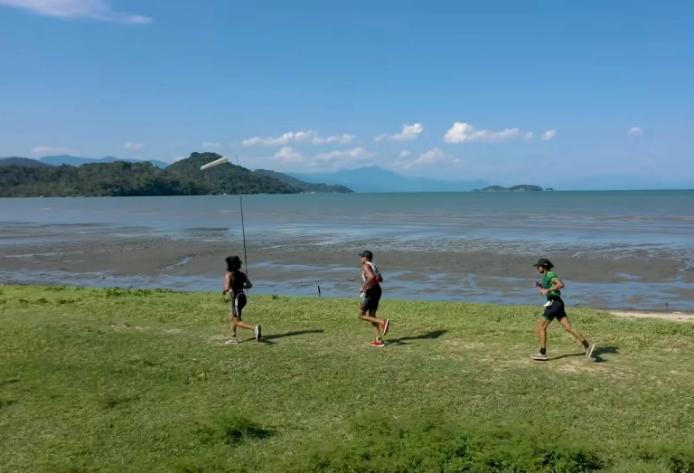 Três pessoas correndo na margem de uma praia em dia ensolarado em Paraty