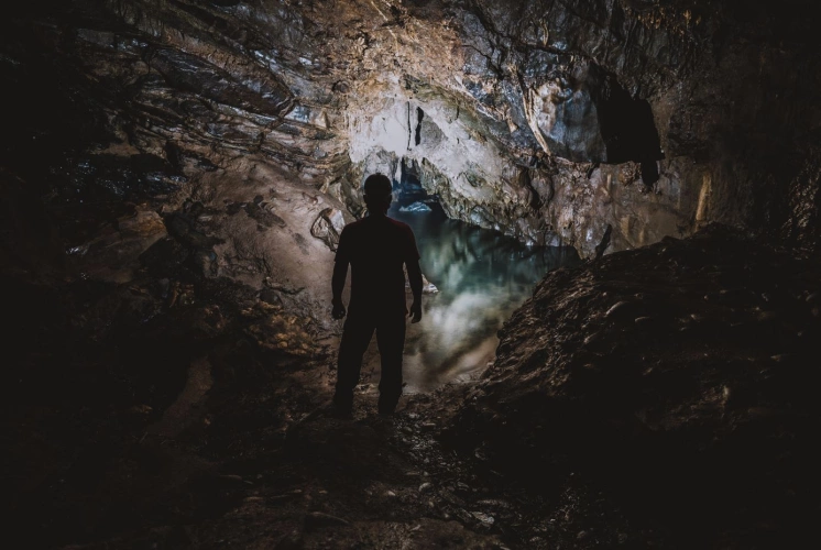 Homem de capacete com lanterna em pé em meio às estruturas de uma caverna escura