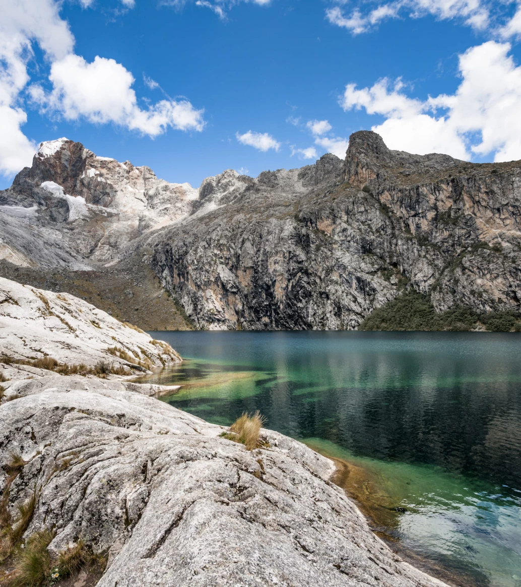 Lagoa com água verde-esmeralda em meio a formações rochosas em dia ensolarado na área dos Andes, no Peru.