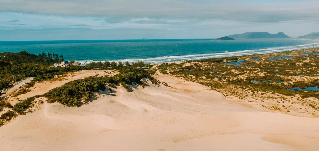 Vista panorâmica de praia deserta de águas azuis cercada por dunas e vegetação