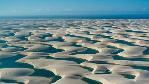 Vista panorâmica do Parque Nacional dos Lençóis Maranhenses com inúmeras lagoas de águas azuis cercadas por dunas de areia em dia ensolarado.