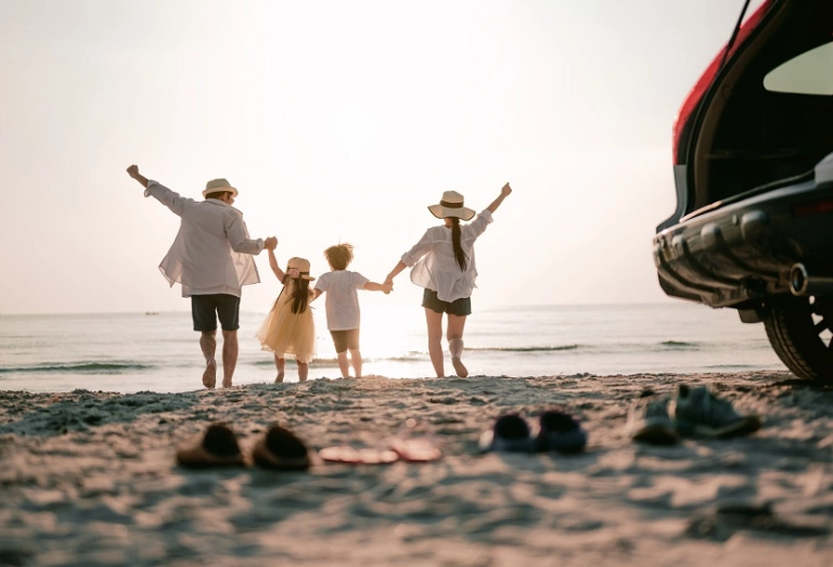família feliz correndo na praia ao pôr do sol. Vista de trás de uma família feliz em uma praia tropical e um carro ao lado. Na imagem, um pai, uma mãe, um garotinho e uma garotinha.
