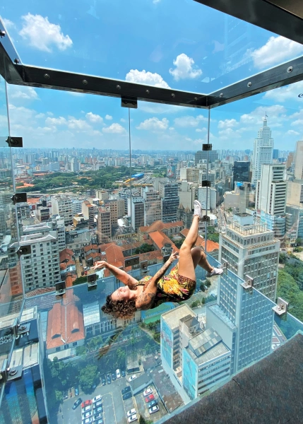 Mulher deitada sobre um deck de vidro no 42º andar de um prédio em São Paulo