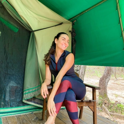 Mel Fronckowiak sorrindo sentada em cadeira dentro de tenda localizada no cerrado em dia claro.