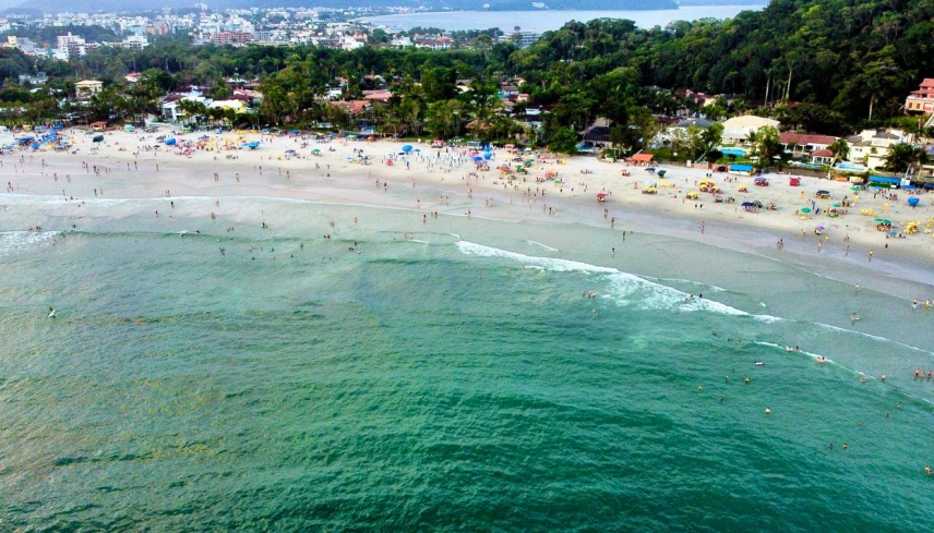 Praia do Tenório, Ubatuba (SP). (Foto: Getty Images)Vista aérea de praia central com mar verde-esmeralda, muitos banhistas e barracas na areia. Há casas e vegetação à beira mar