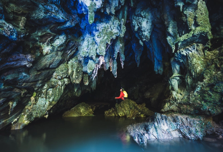 Homem dentro de uma caverna sentado em uma estrutura rochosa e observando as estalactites no teto