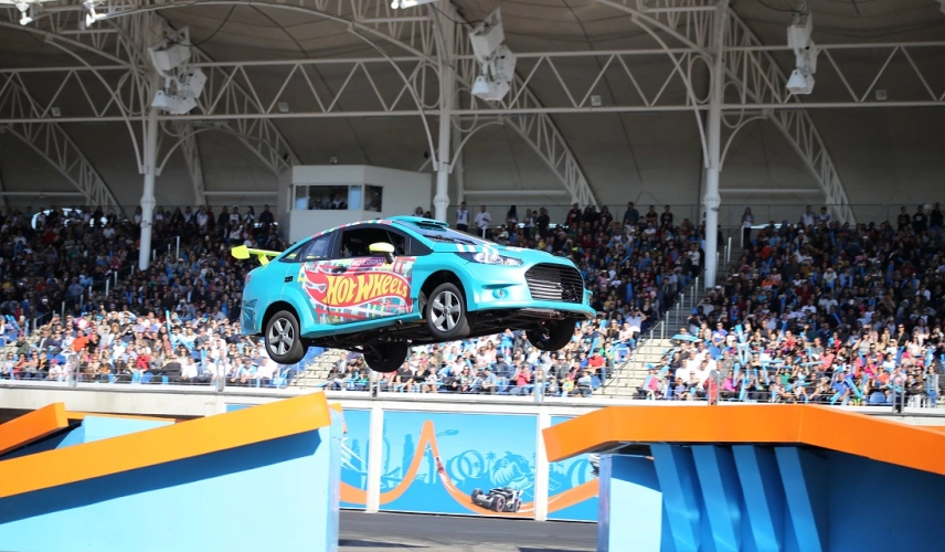 Um carro azul parado no ar em demonstração para um público de várias pessoas