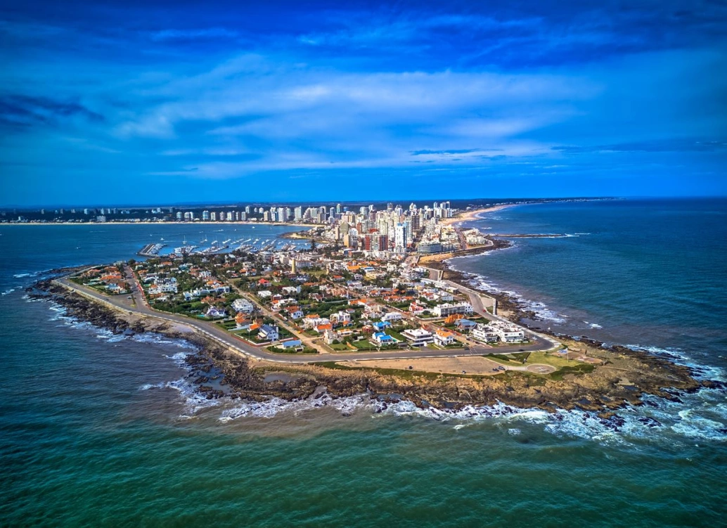 Vista aérea de uma península no Uruguai. Na porção de terra cercada por água, há ruas asfaltadas, casas e prédios