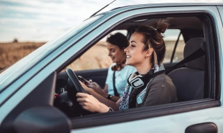Mulher jovem dirige um carro com a amiga ao lado.