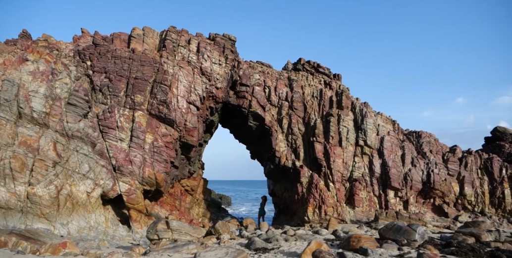 Mulher em pé dentro de buraco em monumento natural formado por pedra em frente ao mar
