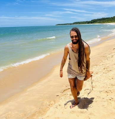 Músico Gabriel Elias sorrindo em praia de águas claras e dia ensolarado