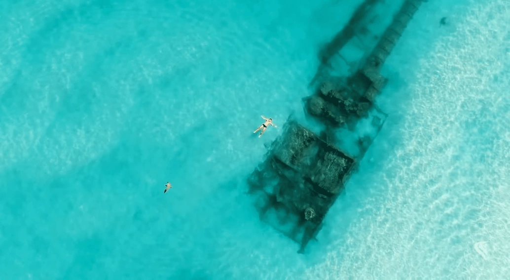 Praia de água azul turquesa com embarcação naufragada na profundidade