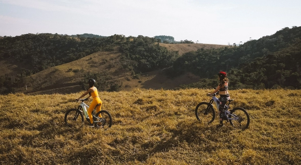 Duas mulheres passeando de bicicleta em zona rural com vegetação ativa
