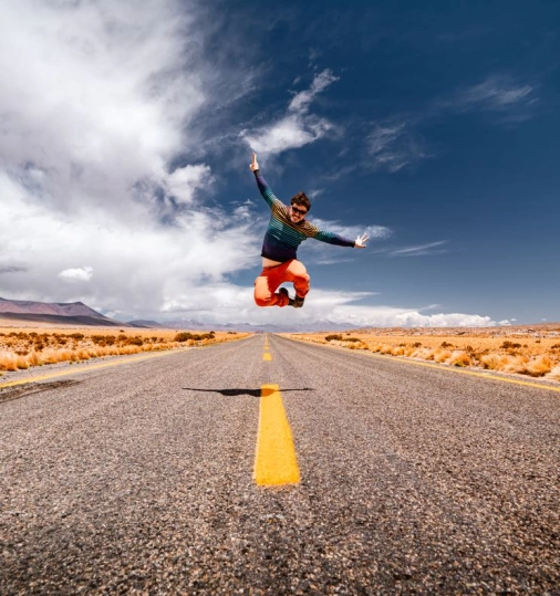 Homem pula para foto em meio a uma rodovia vazia no deserto.