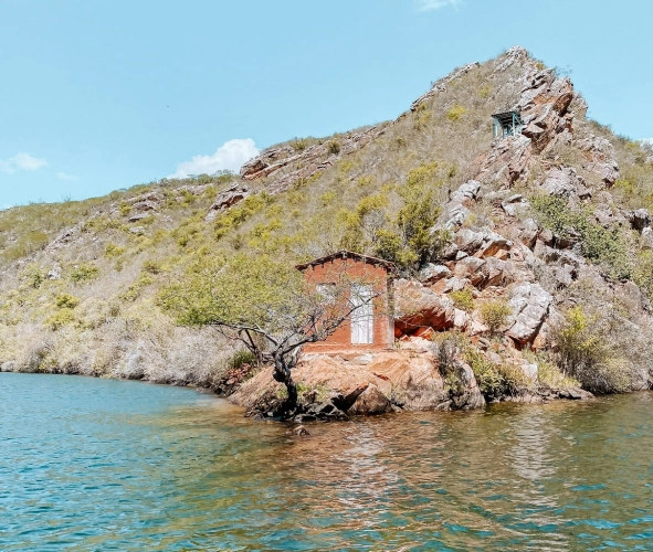 Uma pequena casa construída sobre pedras de uma montanha cercada por águas de um rio