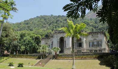 Um palácio em estilo imperial com jardim coberto de grama verde e várias árvores atrás da construção