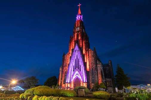 Catedral de Pedra, na cidade de Canela, em estilo gótico,  no Rio Grande do Sul, à noite. Sua fachada está iluminada por luzes de cores vermelha e roxa.