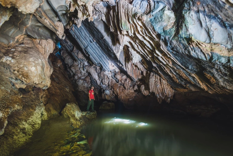 Homem em pé de frente para um poço em meio às estruturas de uma caverna