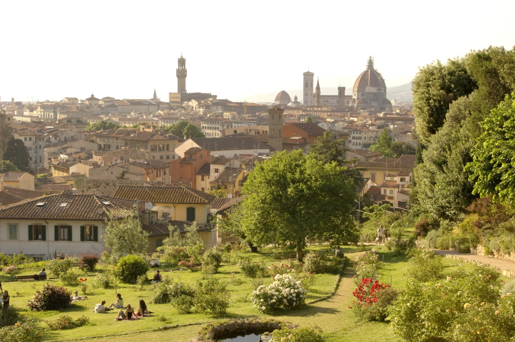 Vista da cidade de Florença, Toscana. Casas tradicionais despontam ao fundo num dia ensolarado, dando destaque a um charmoso parque florido onde pessoas apreciam o dia.