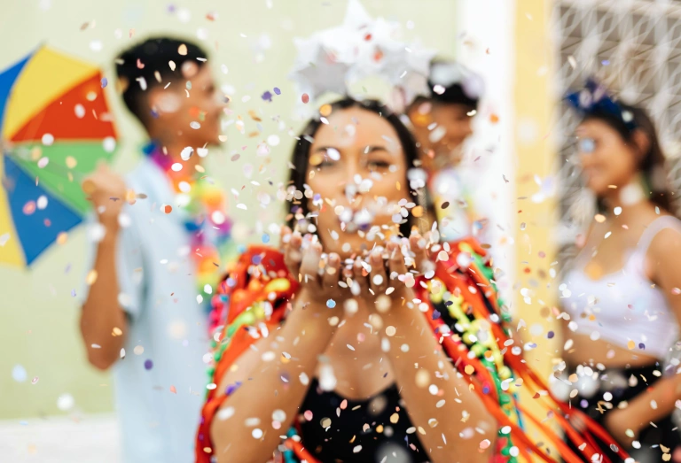 Mulher soprando confetes de papel no Carnaval no Brasil. Há mais três pessoas ao fundo, todas desfocadas