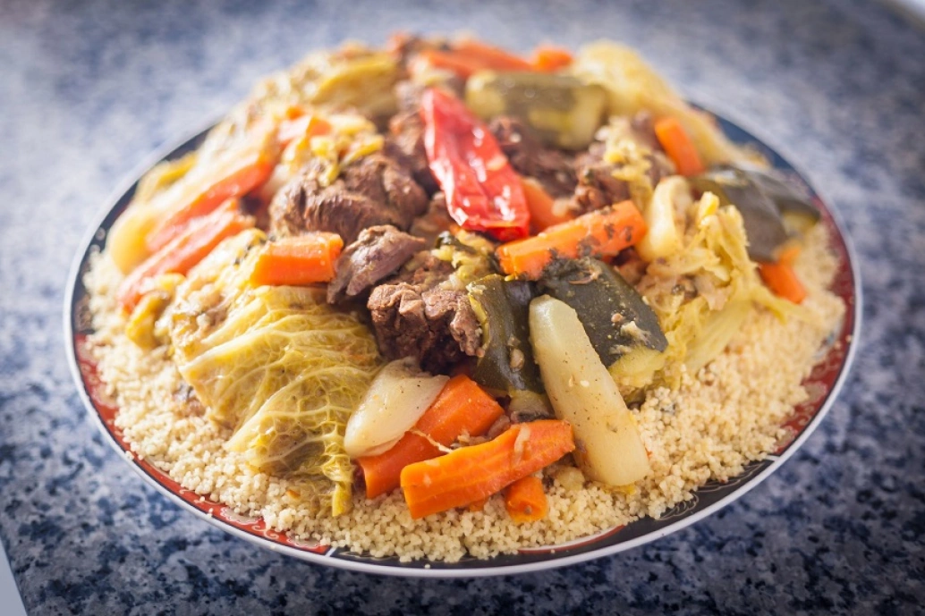 um prato com cuscuz marroquino coberta de legumes cozidos e carne.