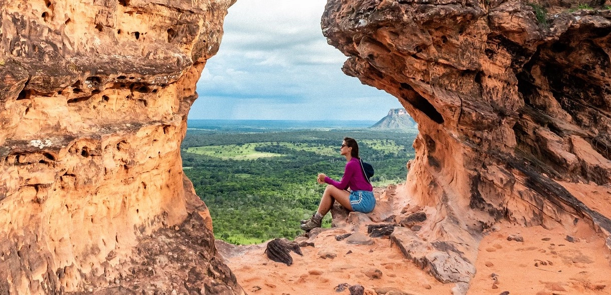 Mulher sentada em formação rochosa vermelho-terrosa aprecia a vista da natureza