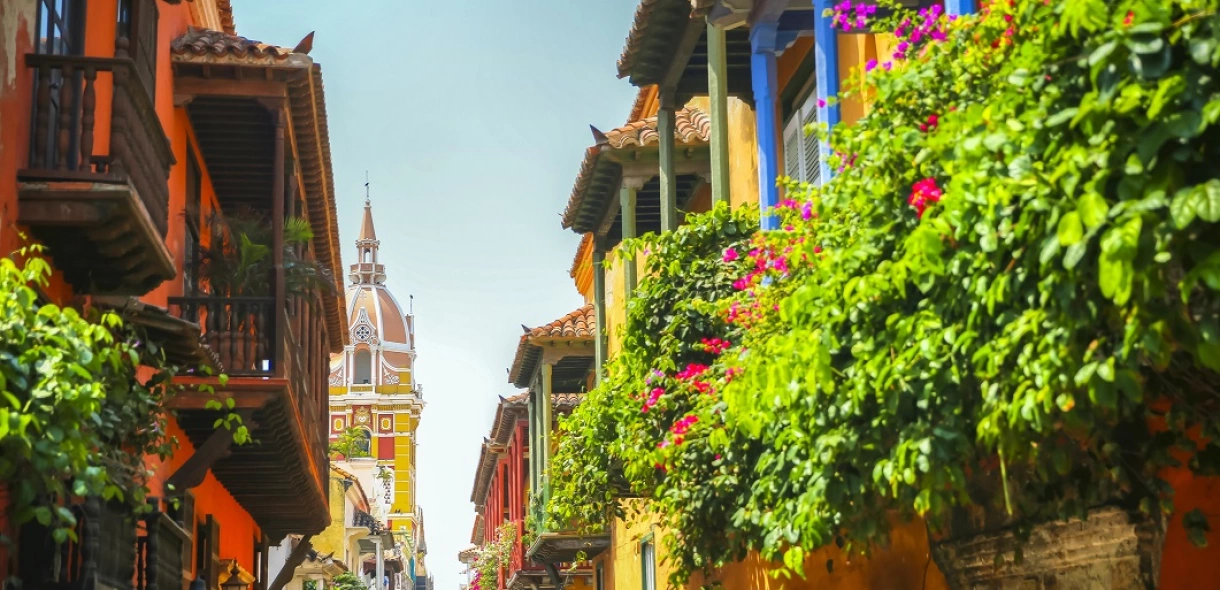Rua com casas coloridas na Colômbia, algumas com plantas em suas varandas e catedral ao fundo
