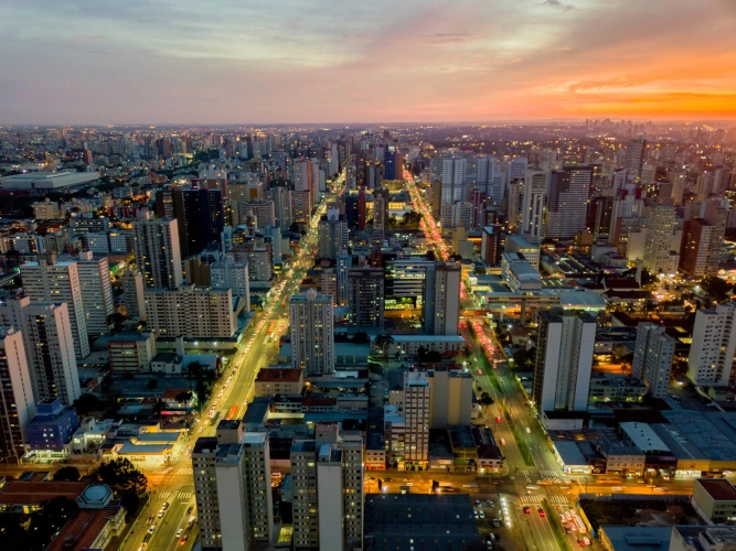 Vista aérea de região urbana em Curitiba durante o entardecer, com as luzes dos carros, das ruas e dos prédios