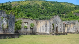 Ruínas de uma antiga construção sobre um gramado. Ao fundo, montanha coberta por vegetação nativa