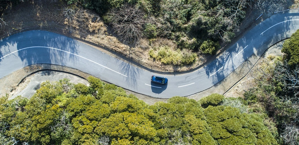 Vista aérea de um carro azul em uma estrada sinuosa.