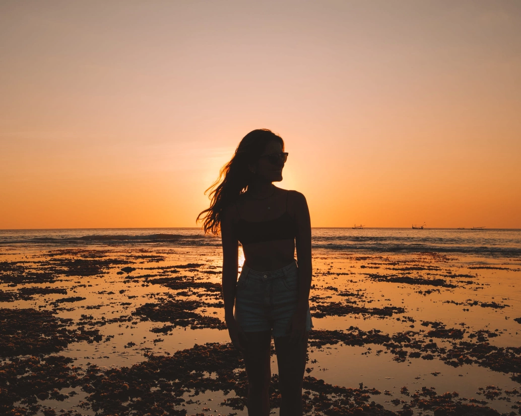 Silhueta de uma mulher na praia com pôr do sol ao fundo