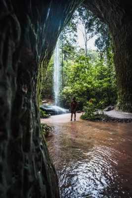 Fotógrafo Fayson Merege em pé dentro de caverna contempla cachoeira e mata verde em dia claro