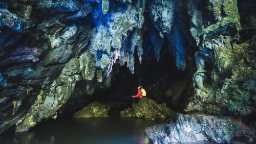 Homem dentro de uma caverna sentado em uma estrutura rochosa e observando as estalactites no teto