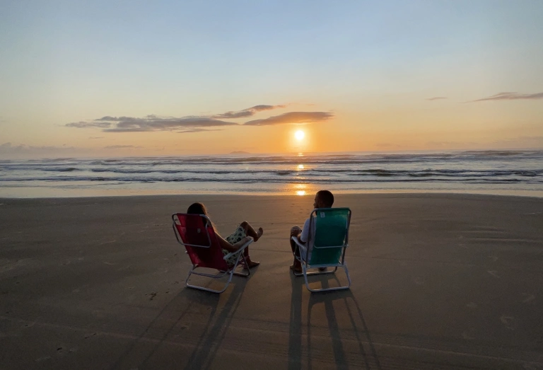 Homem e mulher sentados em cadeira de praia assistem nascer do sol