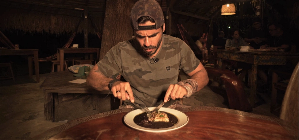 Ricardo Martins sentado à mesa saboreia o prato  Paraensíssimo, que é um peixe de água doce grelhado acompanhado de molho de açaí.