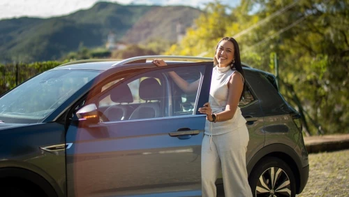 Mulher posa ao lado de carro estacionando em rua em um dia claro