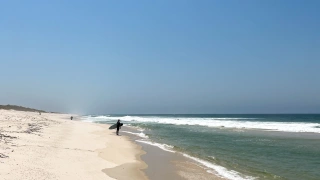 Praia extensa com alguns banhistas na orla em dia ensolarado e céu sem nuvens