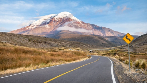 Estrada vazia com curva em direção e um vulcão com topo nevado