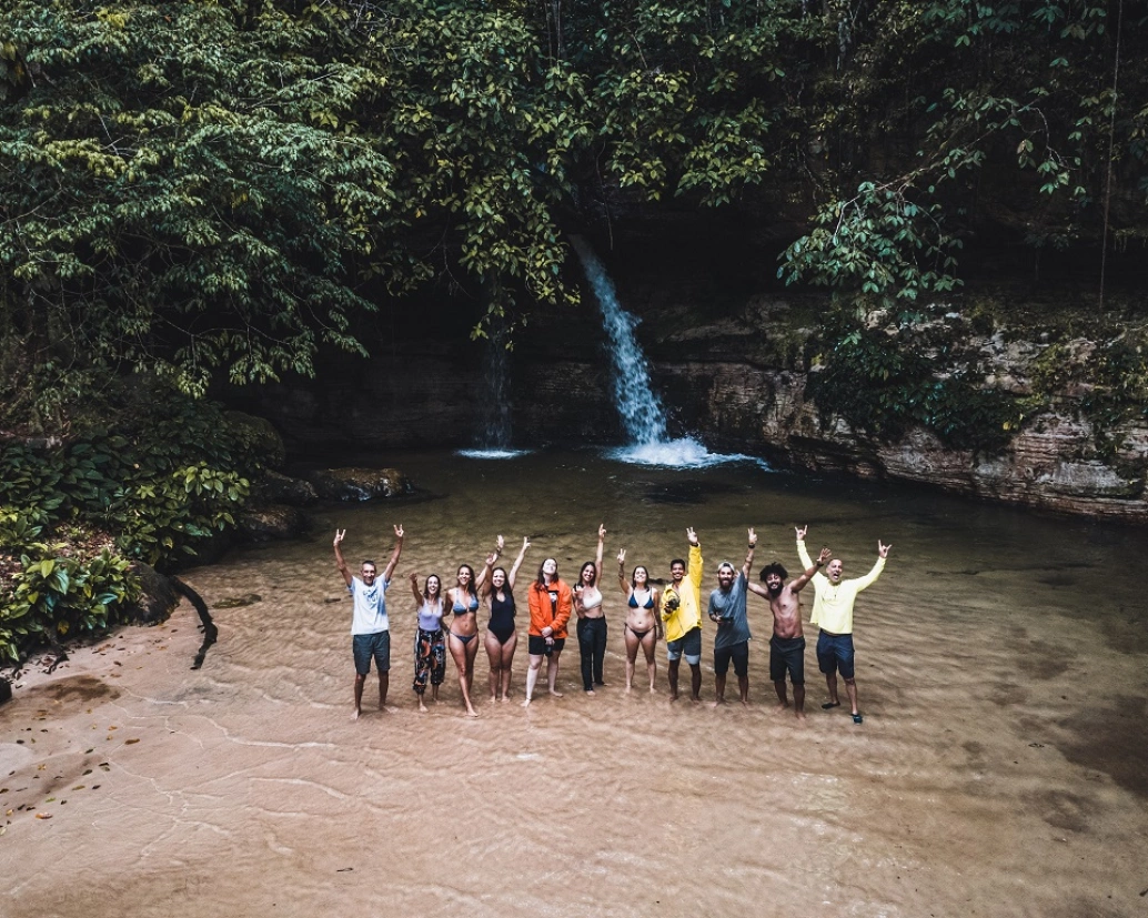 Vários banhistas dentro da Cachoeira da Pedra Furada acenando com mãos ao alto em dia claro