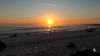 Banhistas assistem pôr do sol em praia de extensa faixa de areia