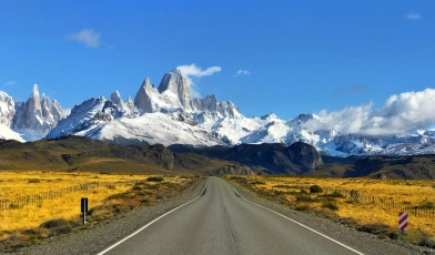 Vista de estrada asfaltada em meio a Argentina. Ao fundo, montanhas enevoadas em dia claro