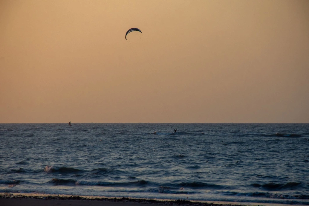 Vista frontal do mal no fim de tarde, céu em tom alaranjado e um banhista praticando kitesurf