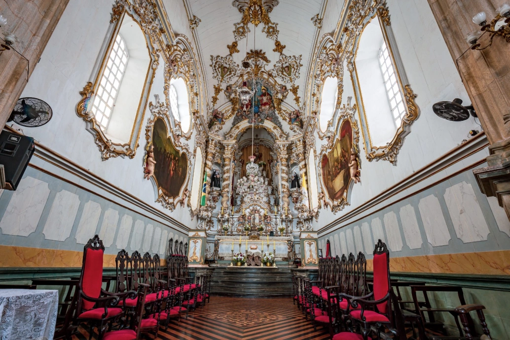 Interior de igreja barroca ornamentada com peças de ouro nas paredes brancas, no teto e no altar