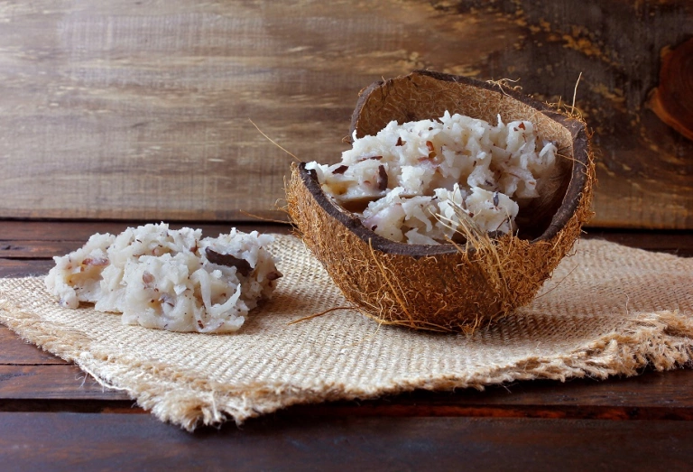 Uma porção de cocada branca, a sobremesa típica brasileira, decorada com a casca do coco sob uma mesa de madeira