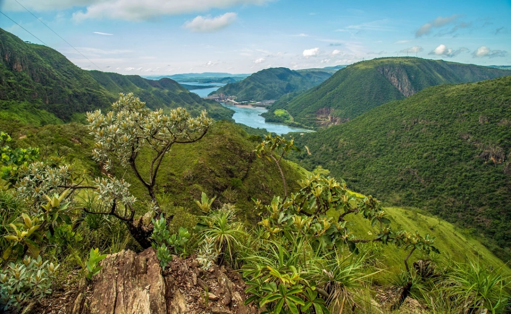 Vista panorâmica do Parque Nacional da Serra da Canastra em MG. Montanhas cobertas por vegetações nativas margeiam um rio sob céu claro.