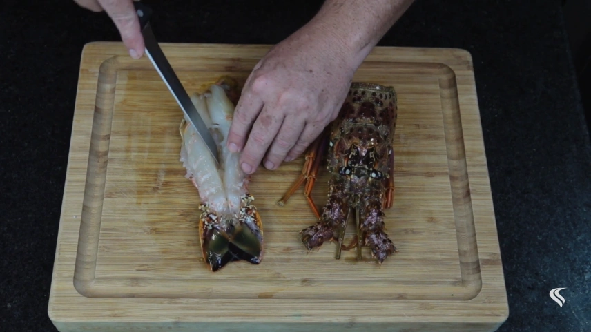 Pessoa limpa lagosta com faca sobre tábua de madeira