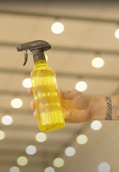 Mão de homem segura recipiente borrifador com líquido amarelo transparente.