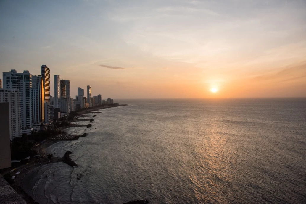 Vista aérea de praia urbana com pôr do sol em Cartagena. A orla da praia é composta por prédios grandes e modernos.